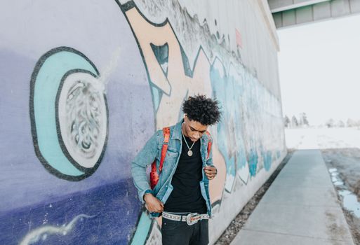 Young man in denim jacket standing by a colorful graffiti wall in Omaha, showcasing modern street style.
