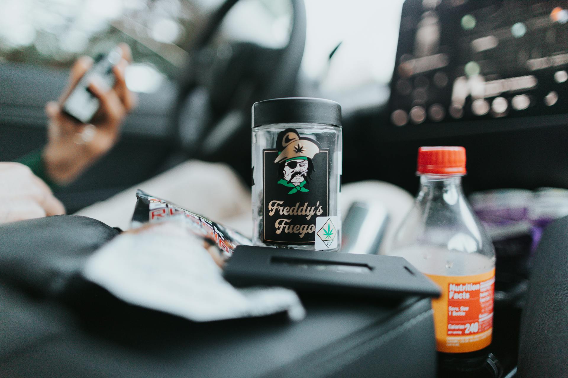 Close-up of cannabis jar and drink bottle in a car interior for lifestyle or product content.