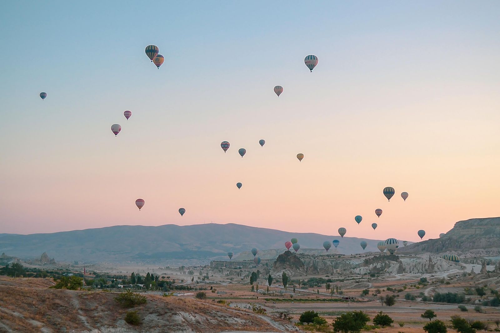 Hot-air balloons drifting over a valley at sunset — photo by Dijital Butik on Pexels
