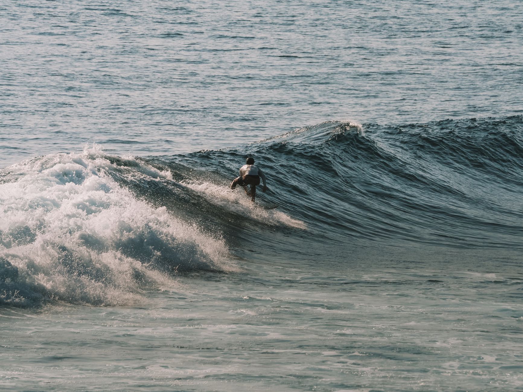 A surfer catches a wave in the clear waters off Bali, Indonesia, showcasing the thrill of ocean sports.