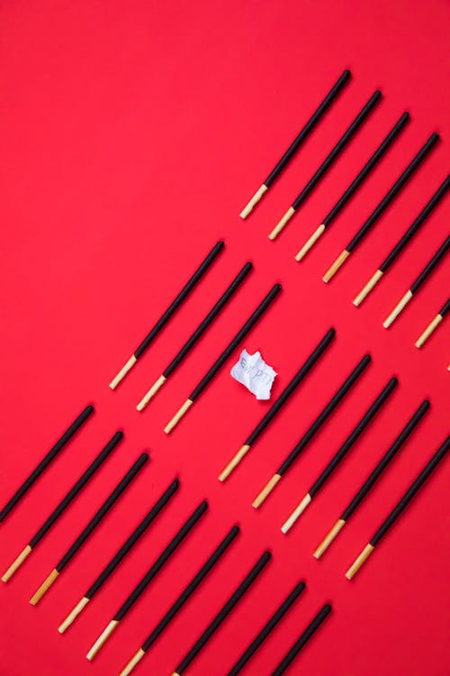 From above of many identical wooden food sticks in rows with piece of paper on bright background