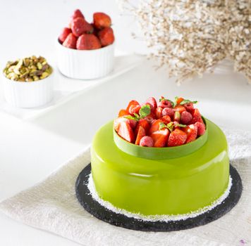 From above of delicious cake with bright green shiny icing decorated with sweet strawberries and mint leaves on table
