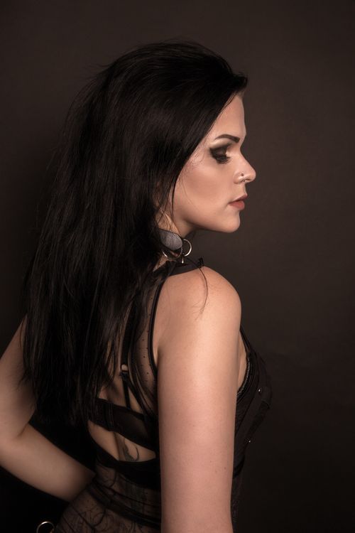Free Artistic side profile portrait of a brunette woman with dark hair and nose piercing against a dark background. Stock Photo