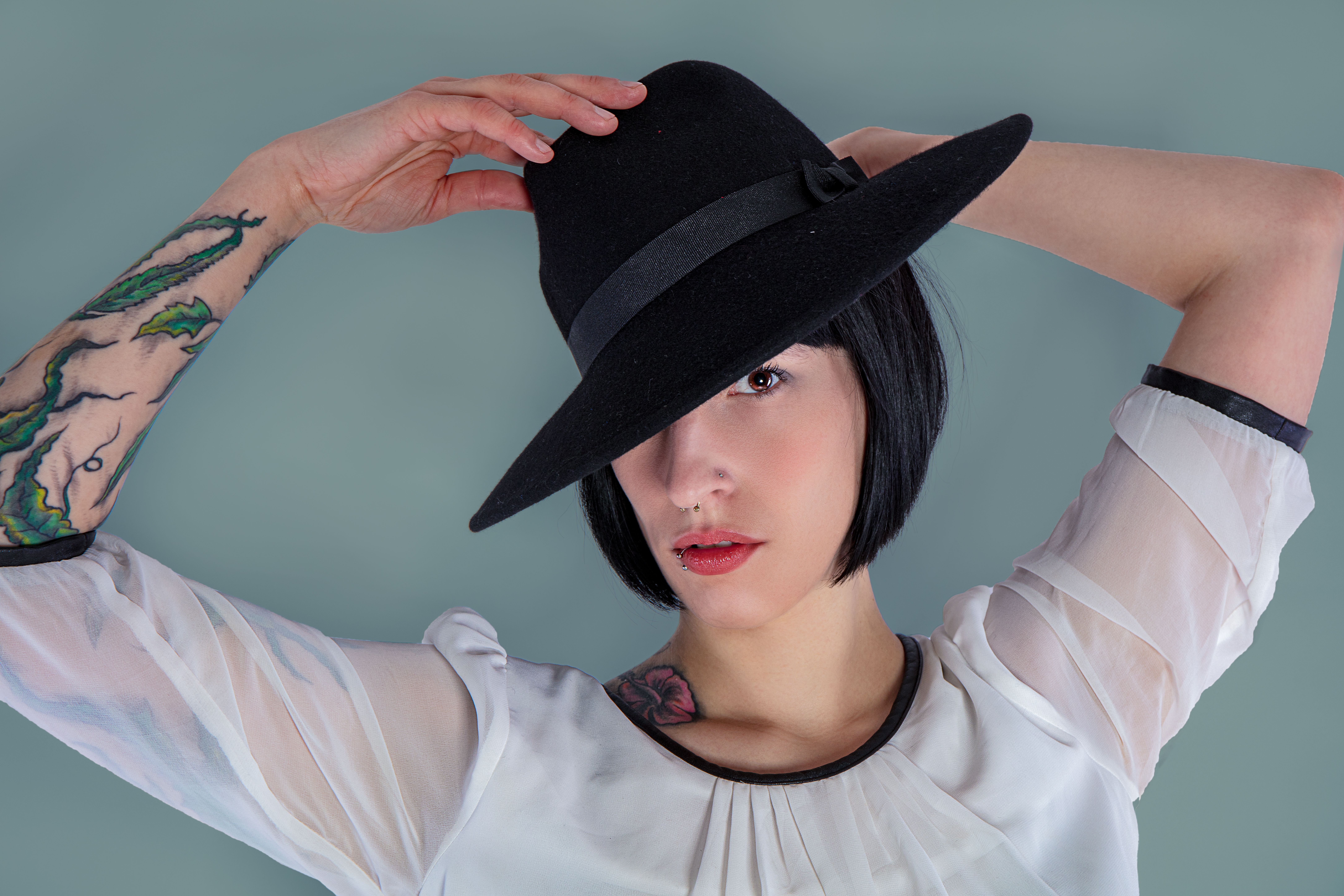 Stylish portrait of a woman with tattoos wearing a black fedora, posing in a studio setting.