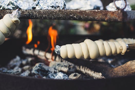 Close-up of twisted bread cooking over a campfire, surrounded by flames and foil-wrapped food.