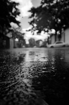 Moody black and white street scene capturing raindrop ripples and reflections in a puddle.