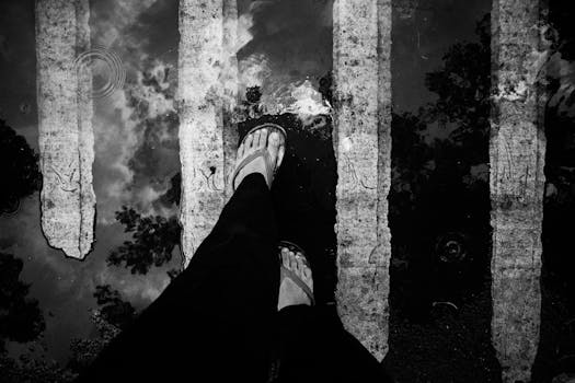 Monochrome shot capturing a foot in flip flops on a wet crosswalk with reflections.