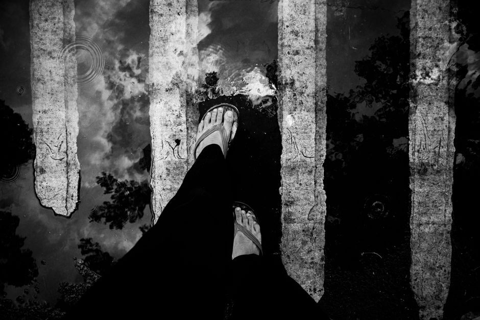 Monochrome shot capturing a foot in flip flops on a wet crosswalk with reflections.