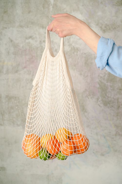 Free Eco-friendly mesh bag filled with oranges and lime, held by a person. Stock Photo