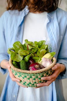 Woman holding a basket filled with fresh vegetables including lettuce, garlic, onions, and cucumbers.