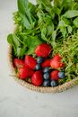 将新鲜的草莓、蓝莓和绿色蔬菜放入编织篮，展示健康的农产品
