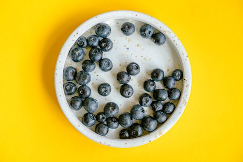 Free Delicious blueberries in rustic ceramic bowl on bright yellow background. Stock Photo