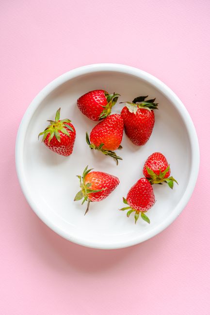 Bright and fresh strawberries in a white bowl with pink background, perfect for food photography.