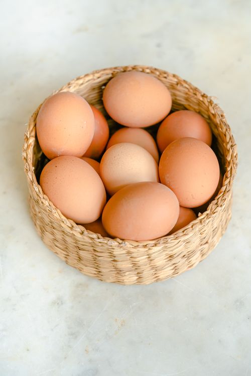 Free High angle shot of brown eggs arranged in a woven basket on a light surface. Stock Photo