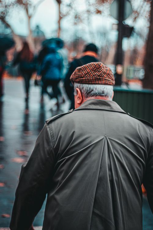 Free From above back view of faceless plump male in felt cap and black wear on wet pavement in town Stock Photo