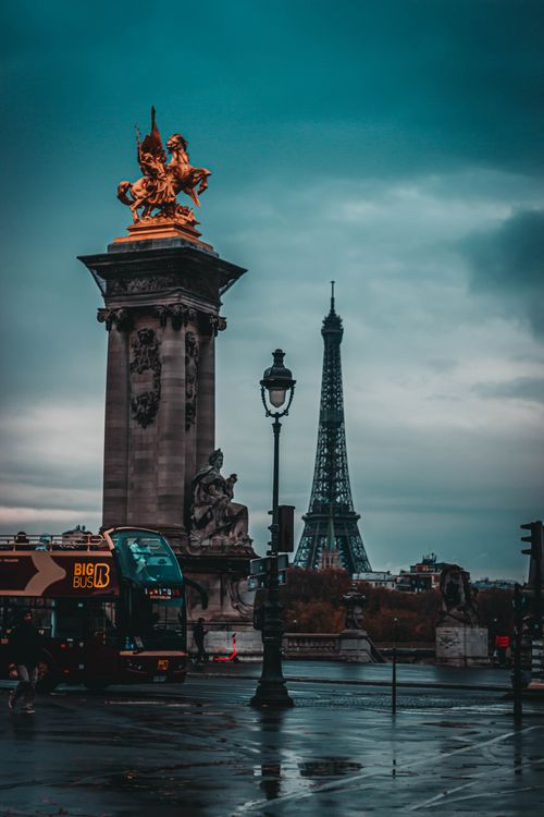 Free From below of aged stone monument with sculptures near metal tower and road under cloudy sky in town at night Stock Photo