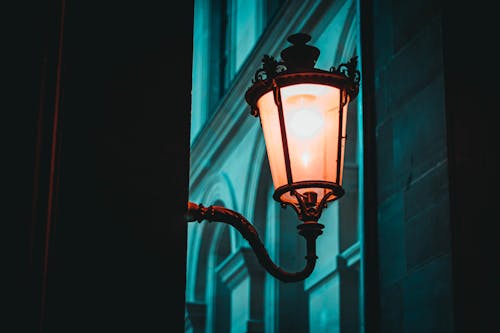 Low angle of creative aged glowing lantern on house wall in city in twilight