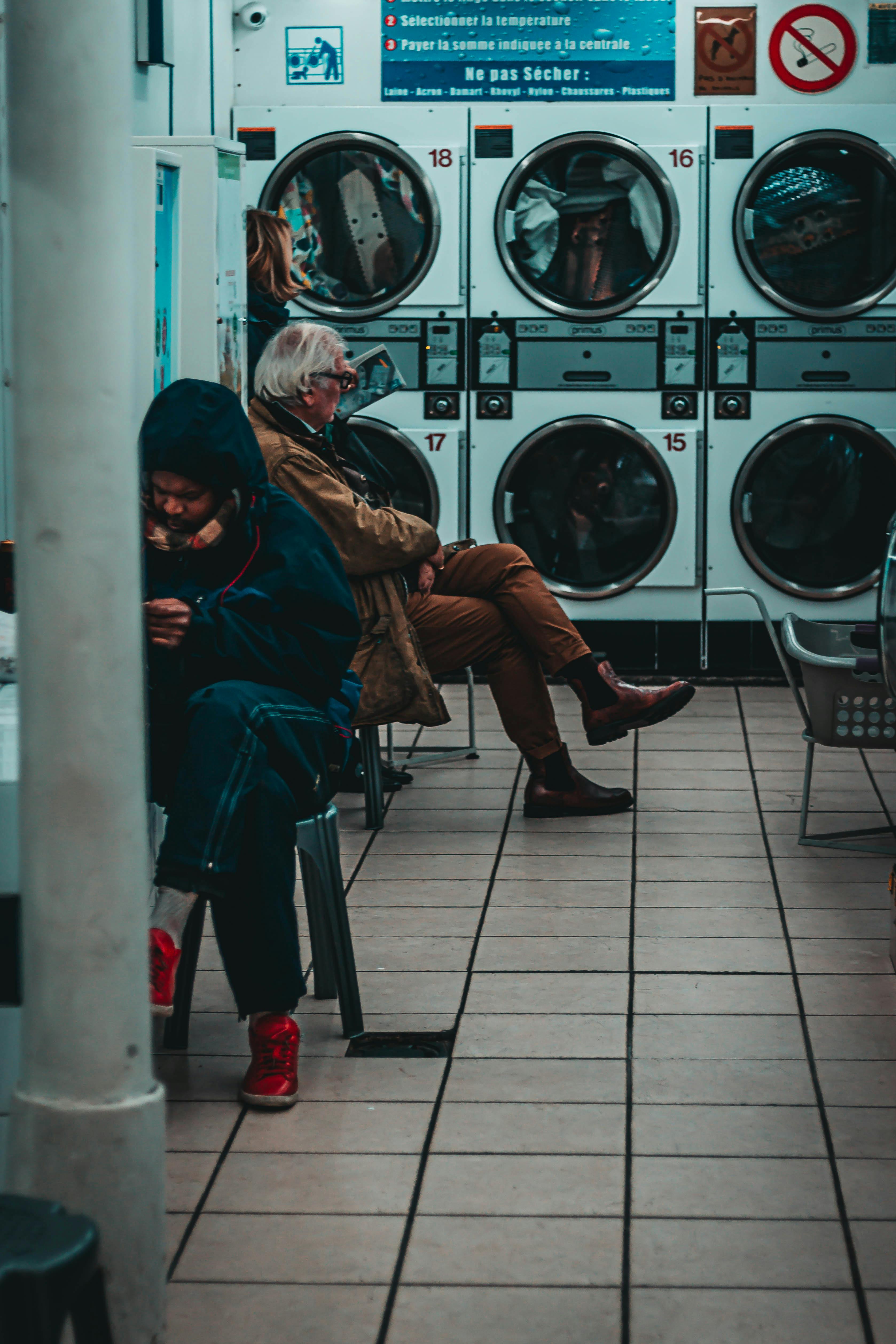 Anonymous people sitting near washing machines in laundromat · Free Stock  Photo