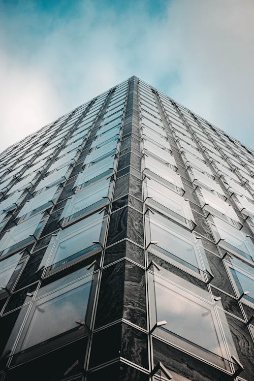 Free Modern skyscraper with glass walls against cloudy sky Stock Photo