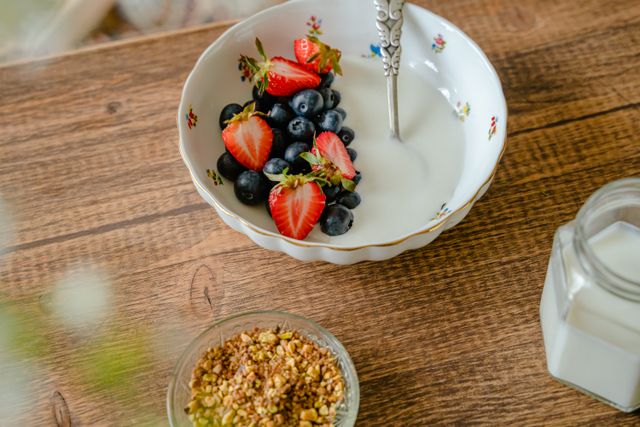 Top view of a breakfast bowl featuring strawberries, blueberries, and yogurt on a wooden table.