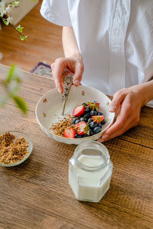 Free Top view of a person preparing a healthy breakfast bowl with fresh berries and granola on a wooden table. Stock Photo