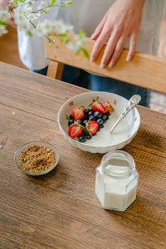 A vibrant breakfast bowl with fresh strawberries and blueberries, served with granola and milk.