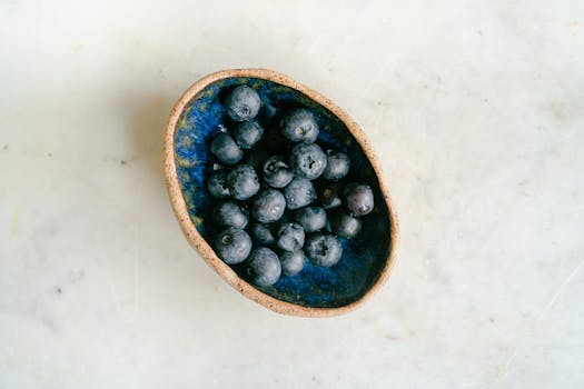 Top view of fresh blueberries arranged in a rustic ceramic bowl on a marble surface.