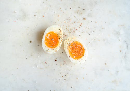 Top view of halved soft boiled egg placed on marble table and spiced with salt and pepper