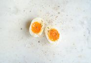 Top view of halved soft boiled egg placed on marble table and spiced with salt and pepper