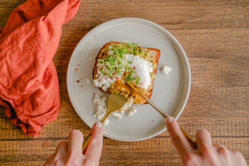 Free Close-up of avocado toast with poached egg, served with a fork on wooden table. Stock Photo
