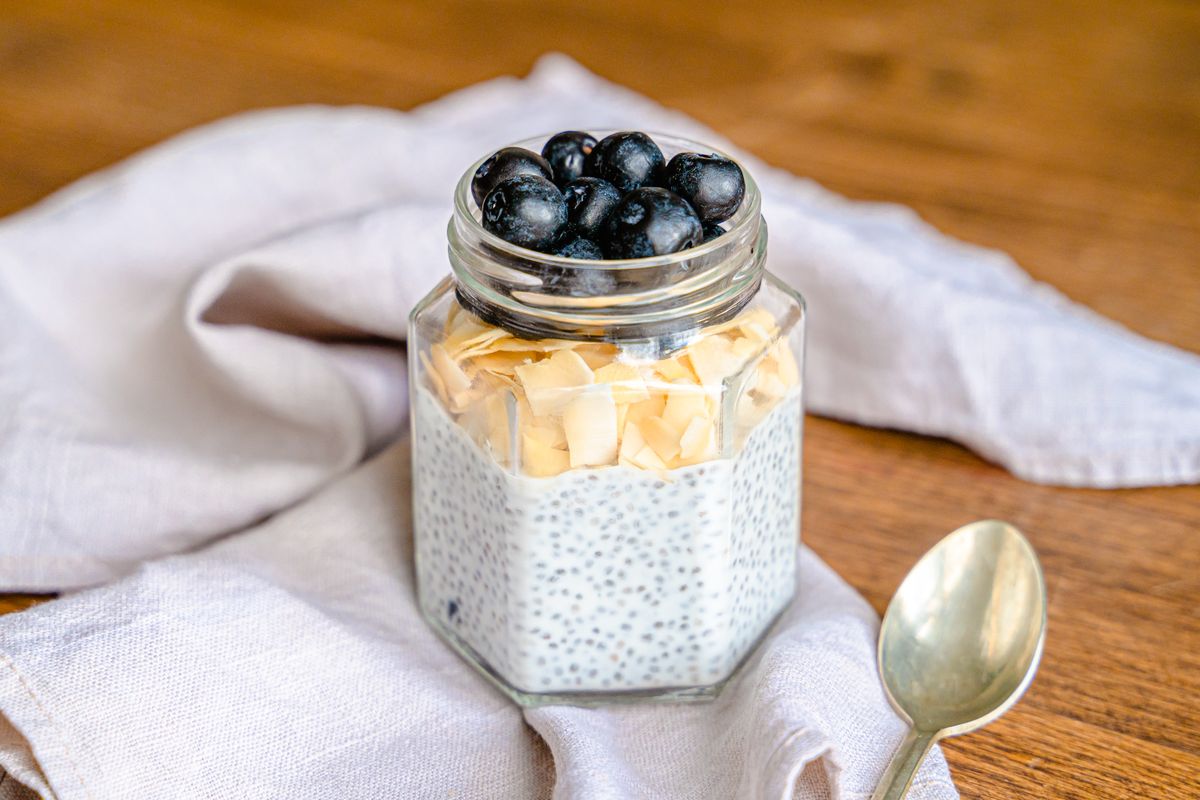 Hexagonal glass jar of white chia pudding topped with toasted coconut flakes and fresh blueberries