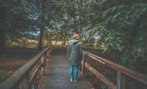 一名女子穿着夹克，独自走在郁郁葱葱的森林里的一座木桥上
