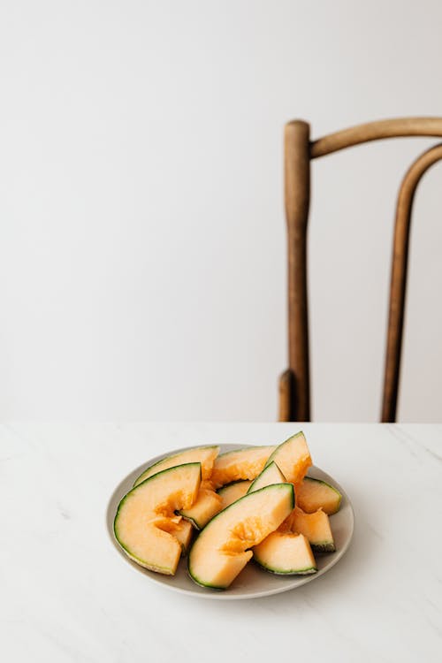 From above plate of fresh ripe sliced melon placed on white table near wooden chair