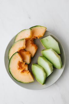 白色盘子上新鲜哈密瓜与蜜露片的俯拍图，非常适合健康饮食