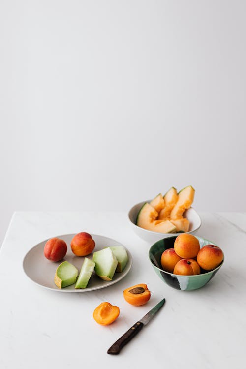 Free Bowl with mixed healthy fruits placed on table with halved apricot and knife Stock Photo