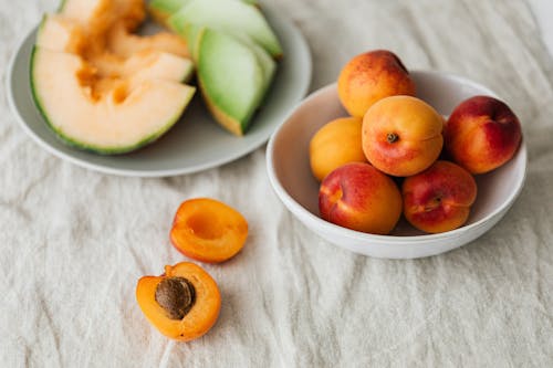 Free Colorful composition of halved apricot placed on natural cloth with bowl of whole ripe fruits and plate of assorted cut melons Stock Photo