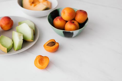 From above of ripe fruits in plate and bowls placed on white marble table