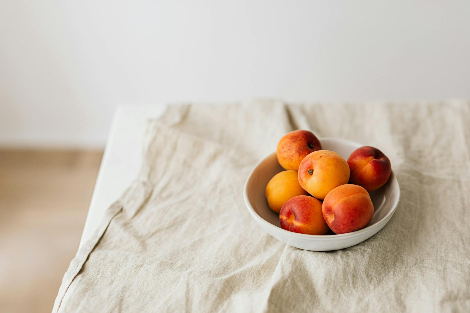 Bunch of ripe apricots in bowl placed on creasy tablecloth on white table