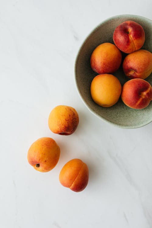 Top view composition of delicious colorful peaches in green ceramic bowl and on white marble table