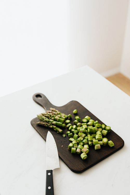 Free From above of chopped fresh green asparagus on wooden board with knife placed on white table in kitchen Stock Photo