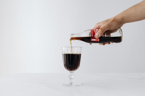 Crop man pouring soda into wineglass on table