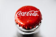 Closeup of red metal bottle cap placed on glass bottle with water droplets on white background