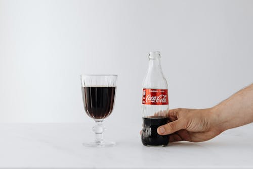 Crop man putting bottle of cola near wineglass on table