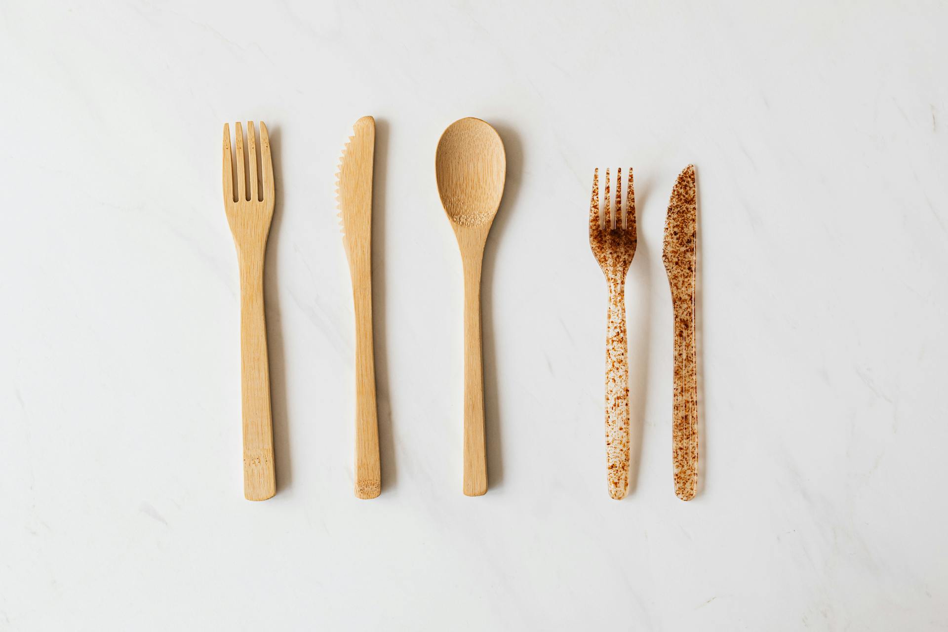 Top view of wooden and plastic cutlery placed in row on white marble table