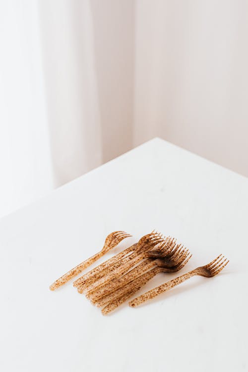 From above of white table with golden in black dots plastic forks placed against beige background and white curtain