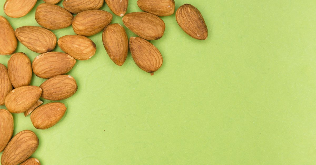 A close-up of almonds scattered on a vibrant green background with ample copy space. - Evidence evidence guide for almond lipid profile randomized trial