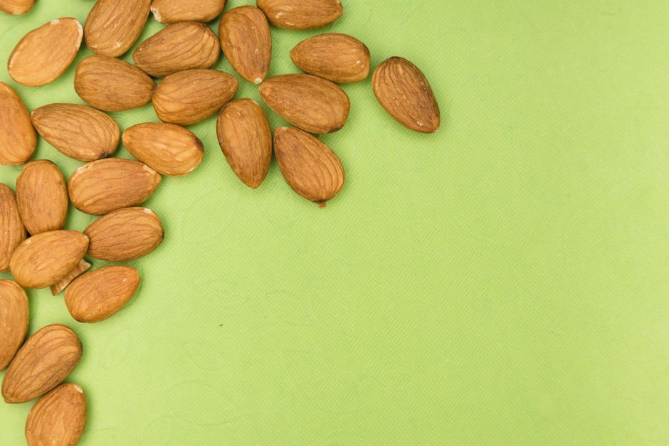 Hạt Hạnh Nhân: "Siêu Thực Phẩm" Cho Làn Da & Vóc Dáng – Cẩm Nang 2026 2 A close-up of almonds scattered on a vibrant green background with ample copy space.