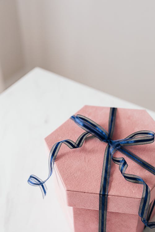 Pink gift box with blue and white striped ribbon on a white table.