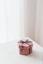From above of blue ribbon tying bow on pink hexagonal gift box placed on white table against beige wall and white curtain