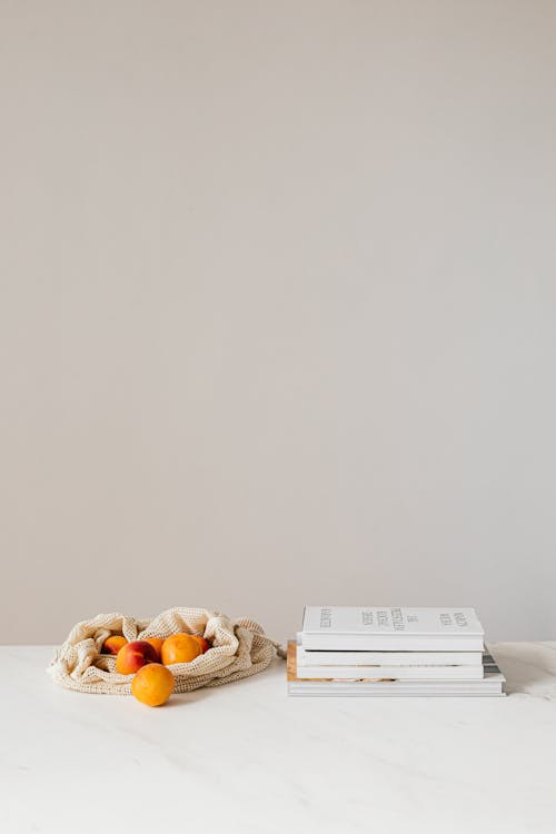 Free Composition of canvas bag with fresh ripe apricots placed on white table near stack of various books Stock Photo